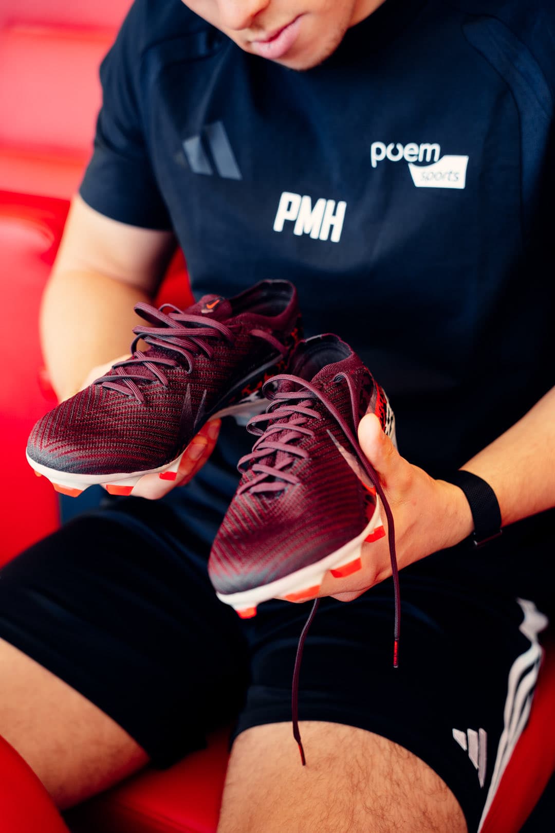 Weinrote Nike-Fußballschuhe in den Händen, nah, dahinter die roten Sitze der MHP Arena
