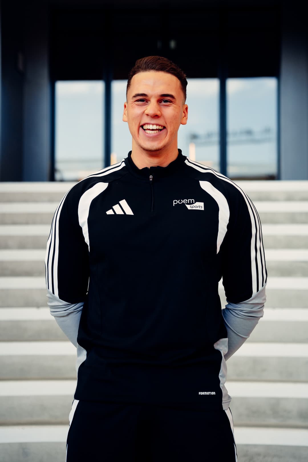 Phil lacht im schwarz-weißen Sweatshirt mit poemsports-Logo aus dem Kit