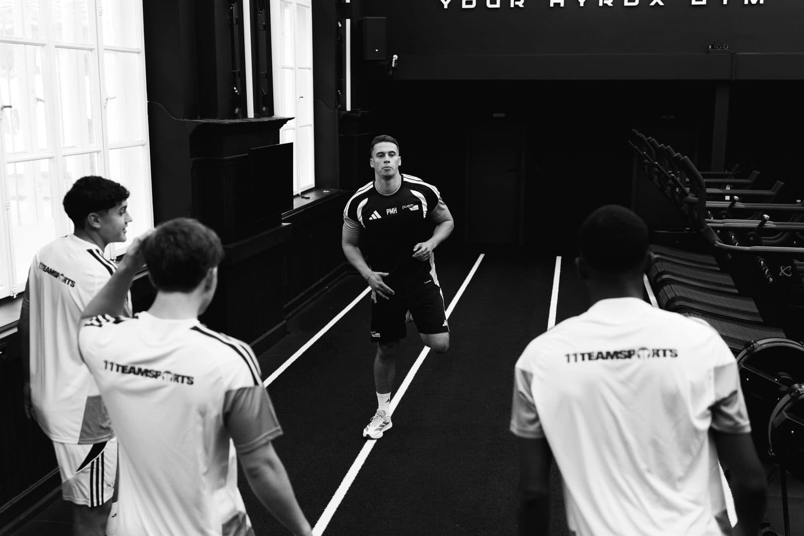 Phil Hernández läuft im Gym auf die Kamera zu, drei Spieler schauen zu